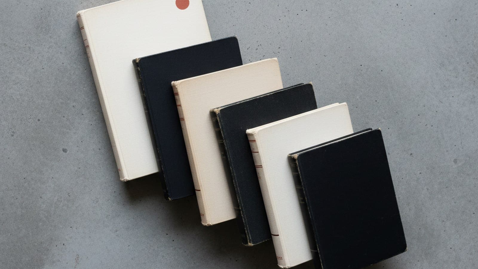 Stack editorial de cinco manuales de marca canónicos del siglo XX — IBM Lufthansa British Rail México 68 NASA dispuestos en orden cronológico sobre concreto